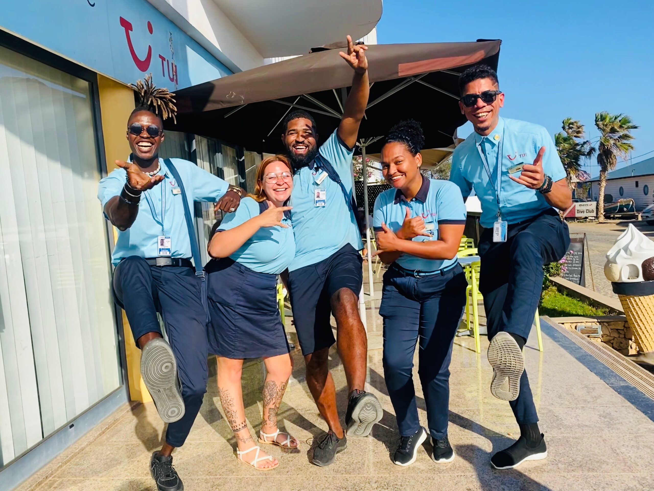 Gruppe von TUI Kollegen in ihrer Uniform, die sich freuen Kundin einer Urlaubsdestination feiern