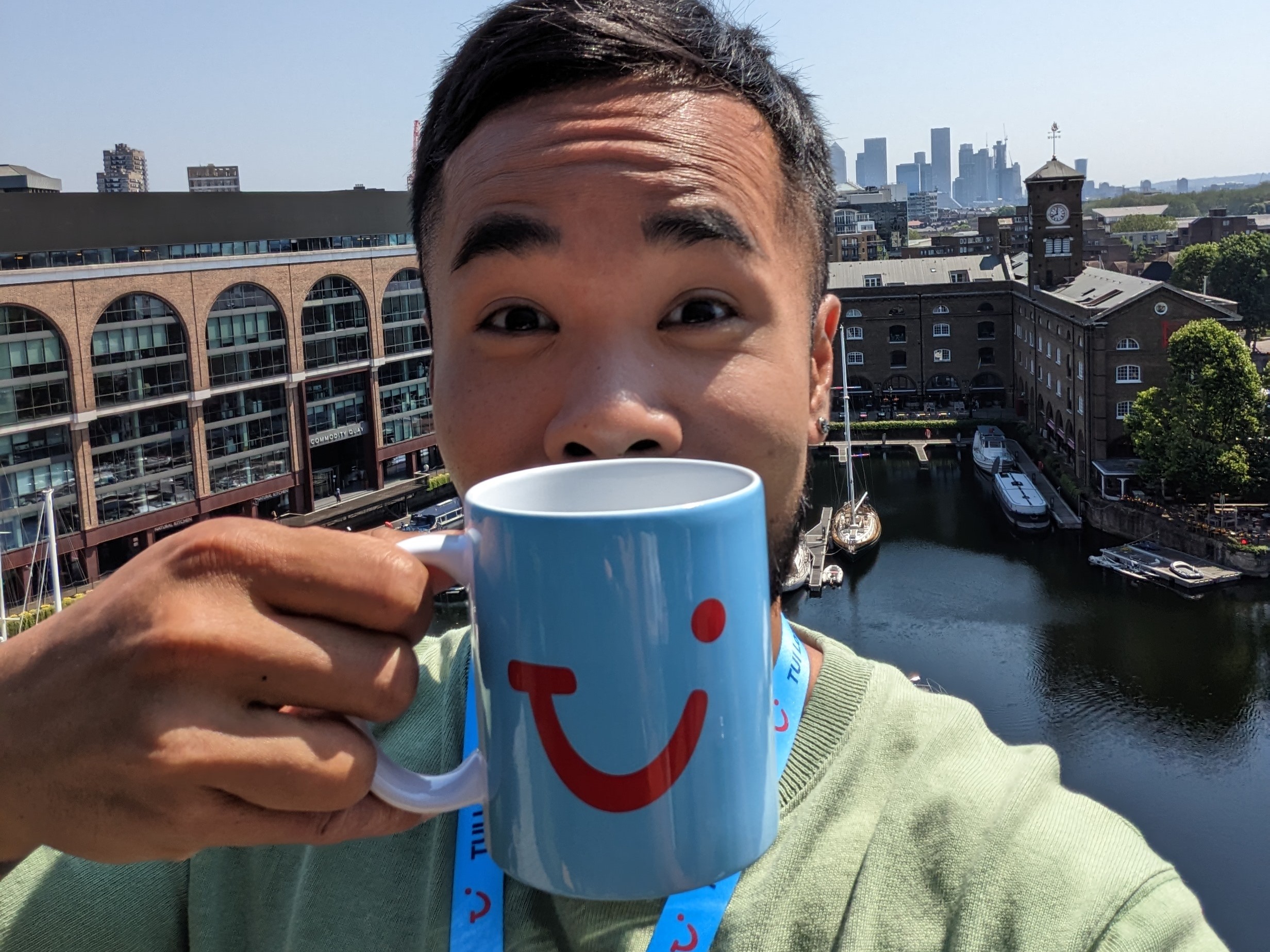 Man holding a mug with a TUI logo on it with some of the london skyline in the background, showing the TUI smile as his own.